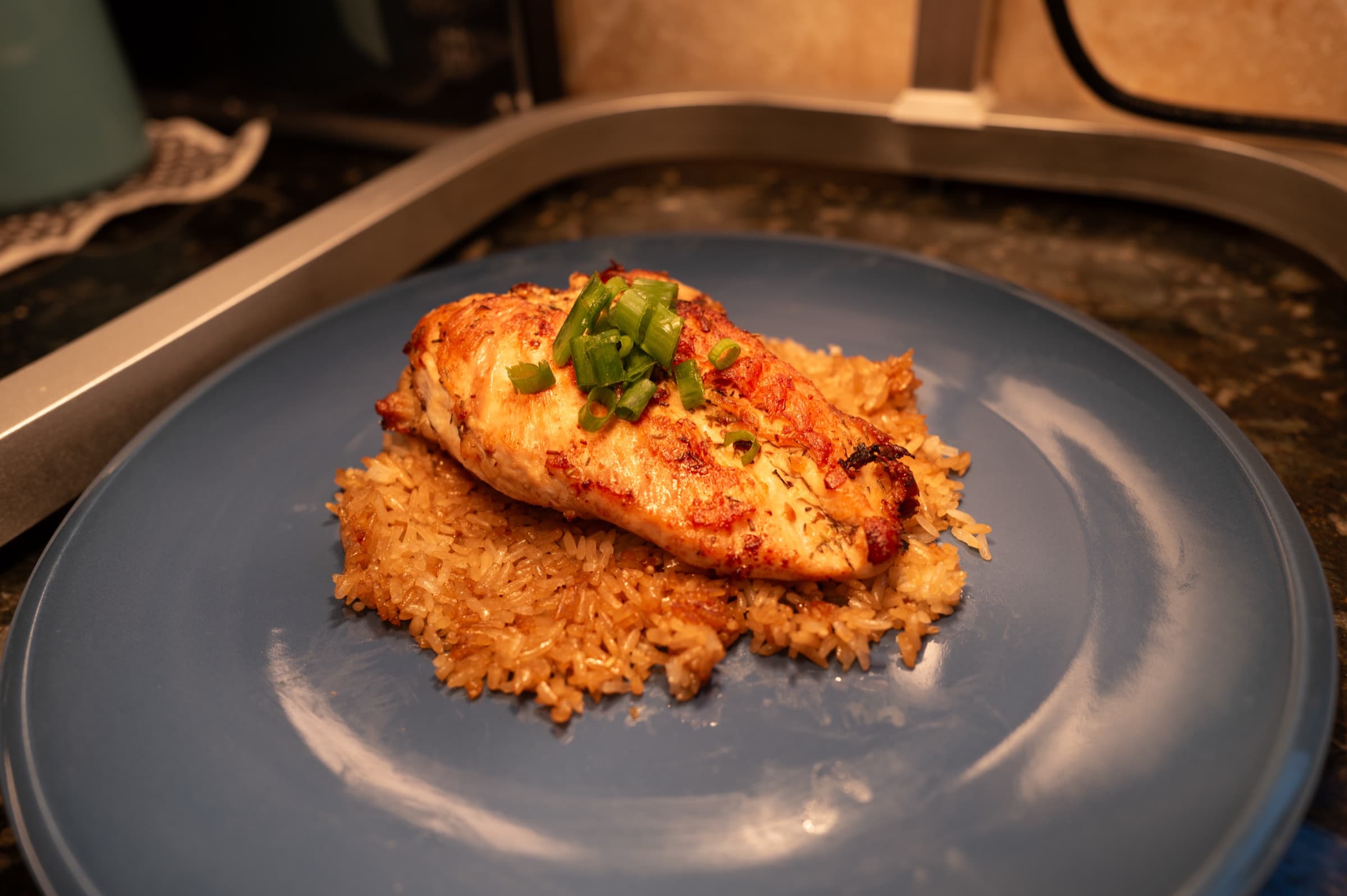 Herb-garnished chicken breast over fried rice on a blue plate