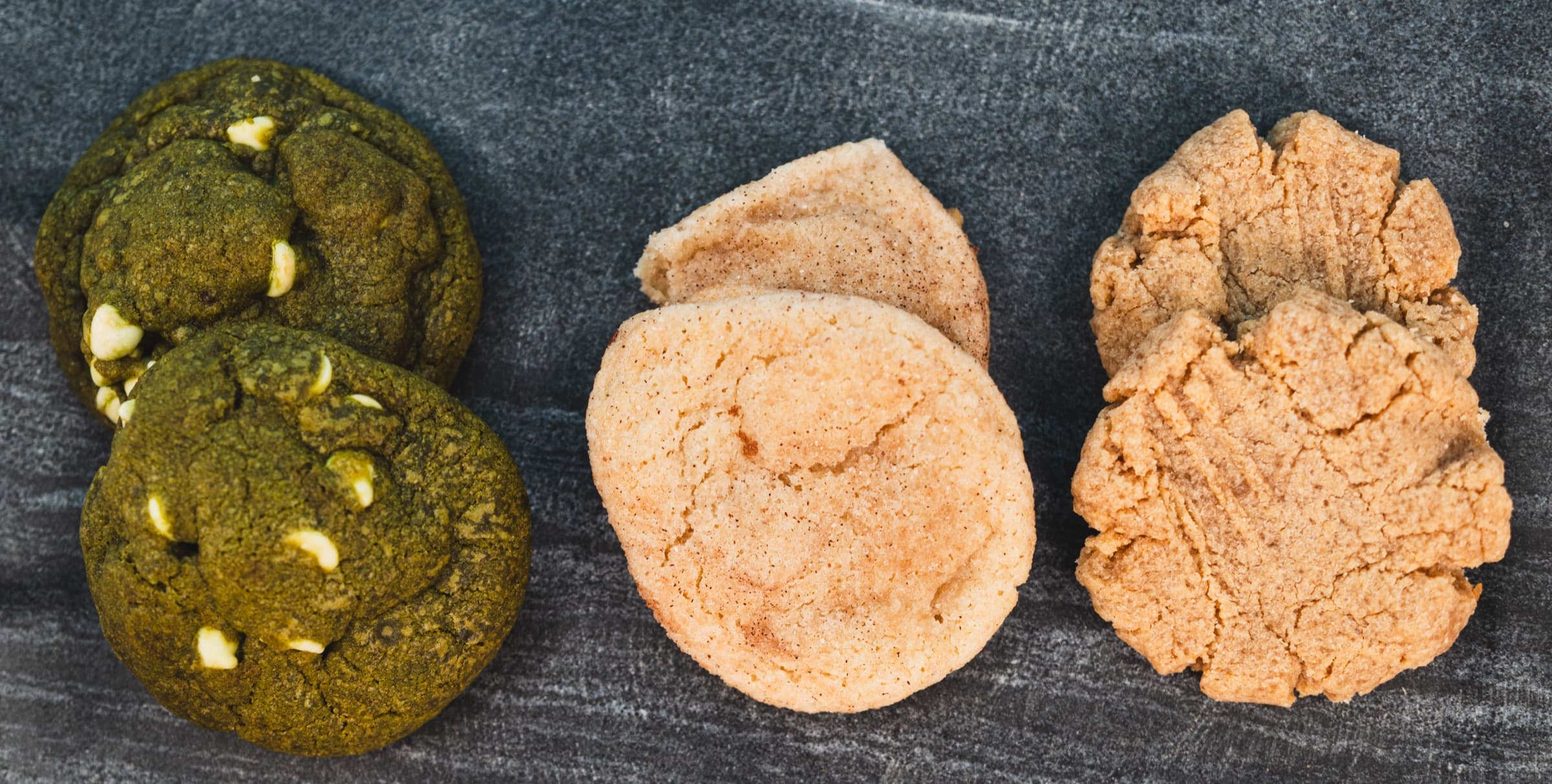 Matcha, snickerdoodle, and peanut butter cookies arranged on slate
