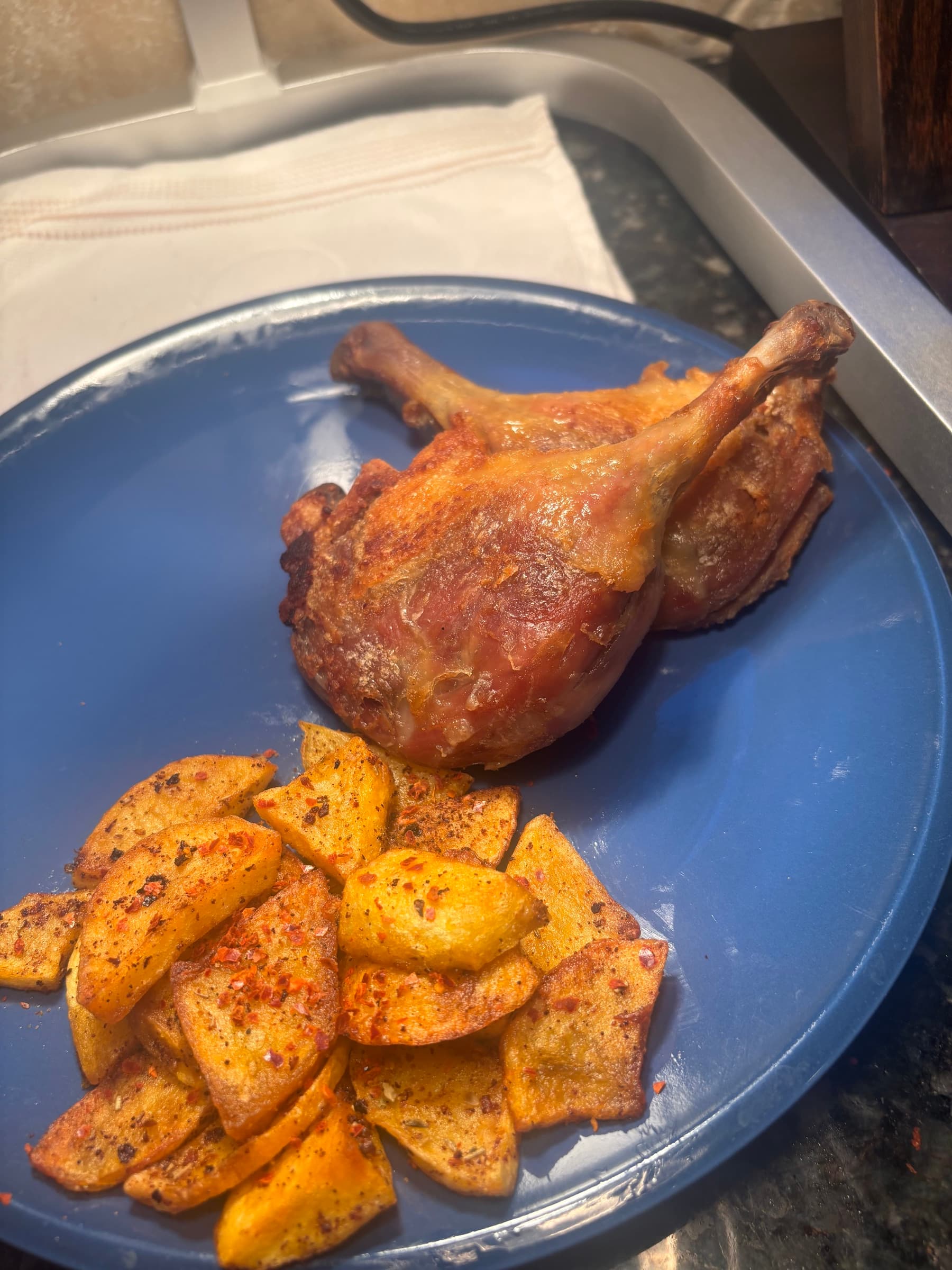 Roasted duck legs with seasoned potato wedges on a blue plate
