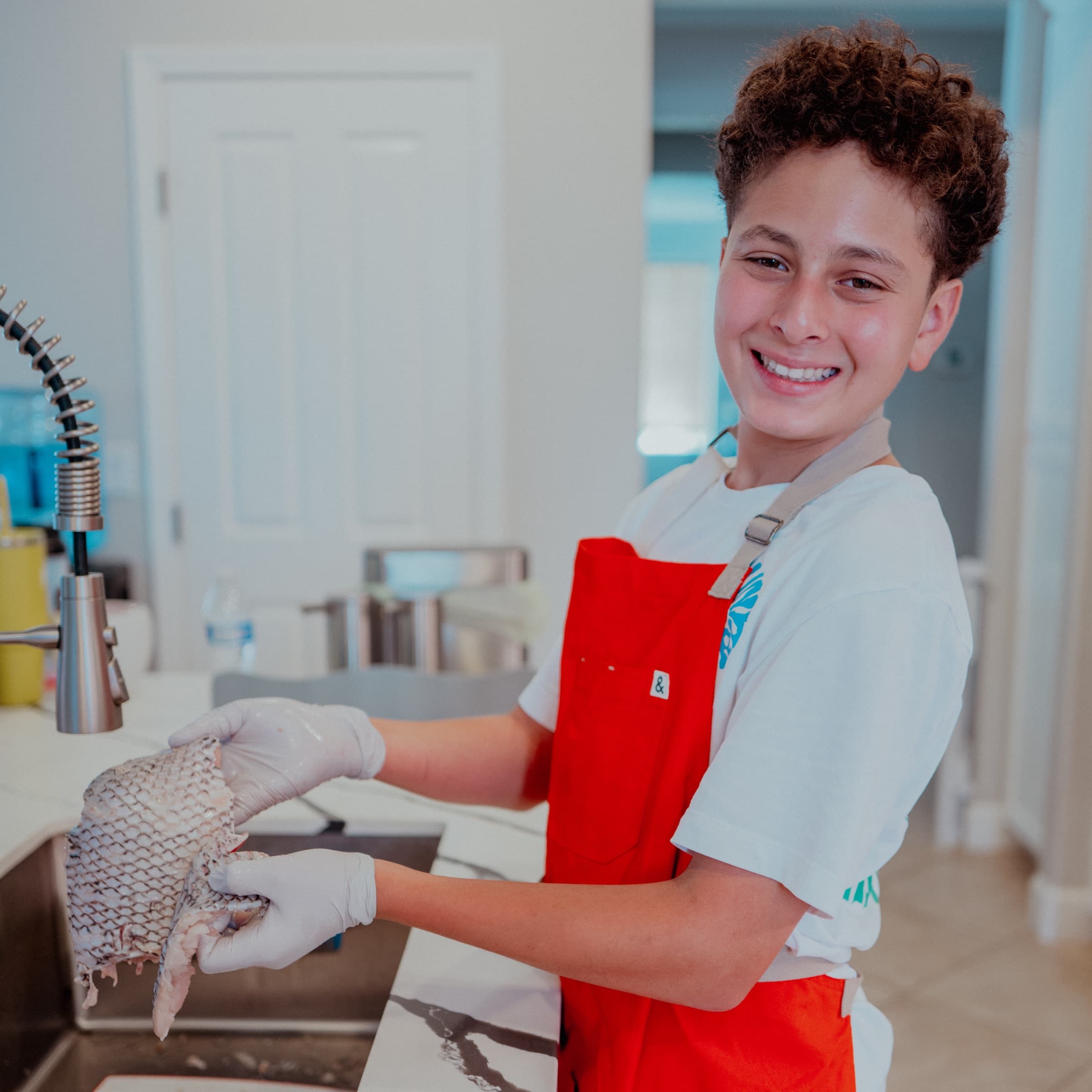 Nour smiling at the kitchen sink while holding a whole fish