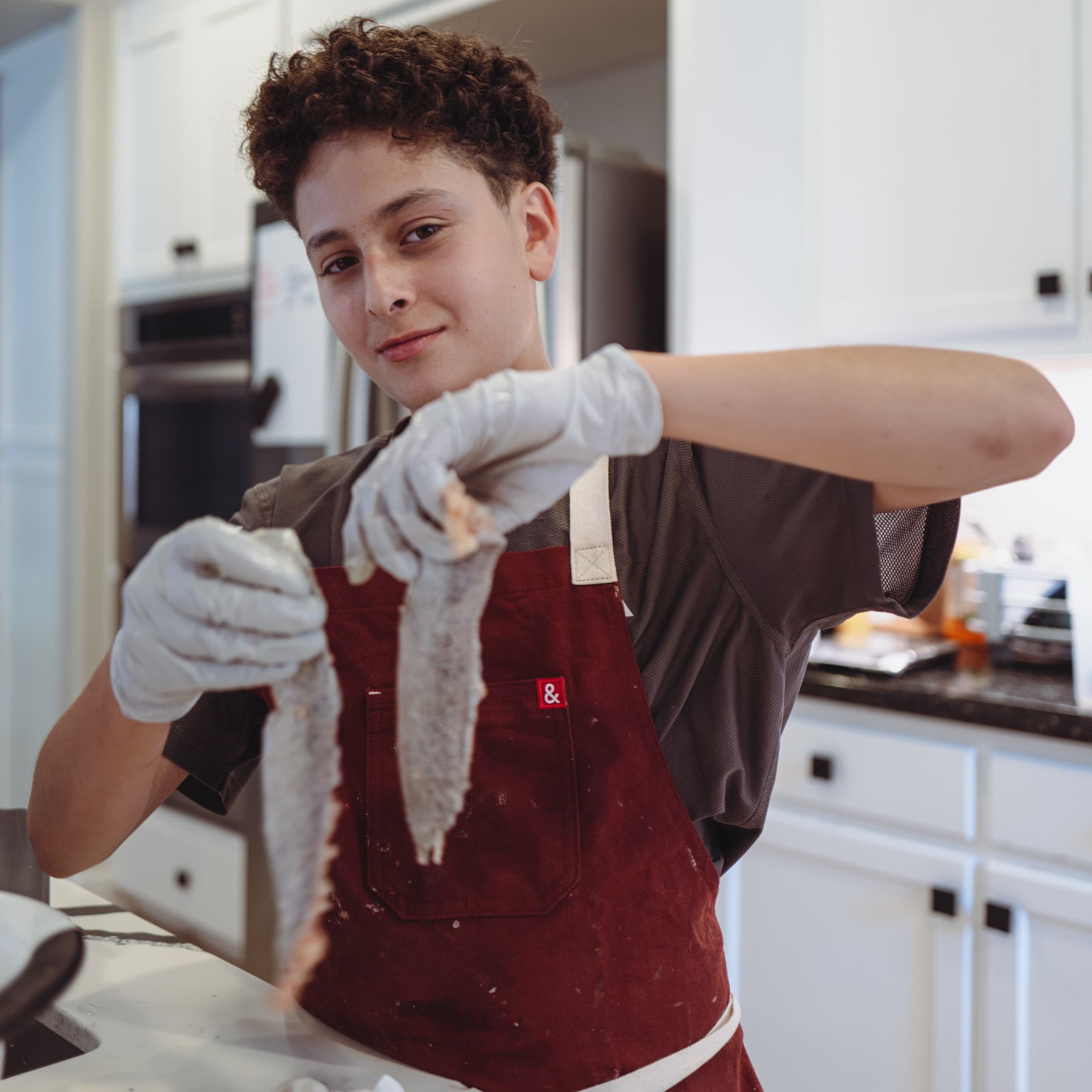 Nour in an apron holding two raw fish fillets in the kitchen