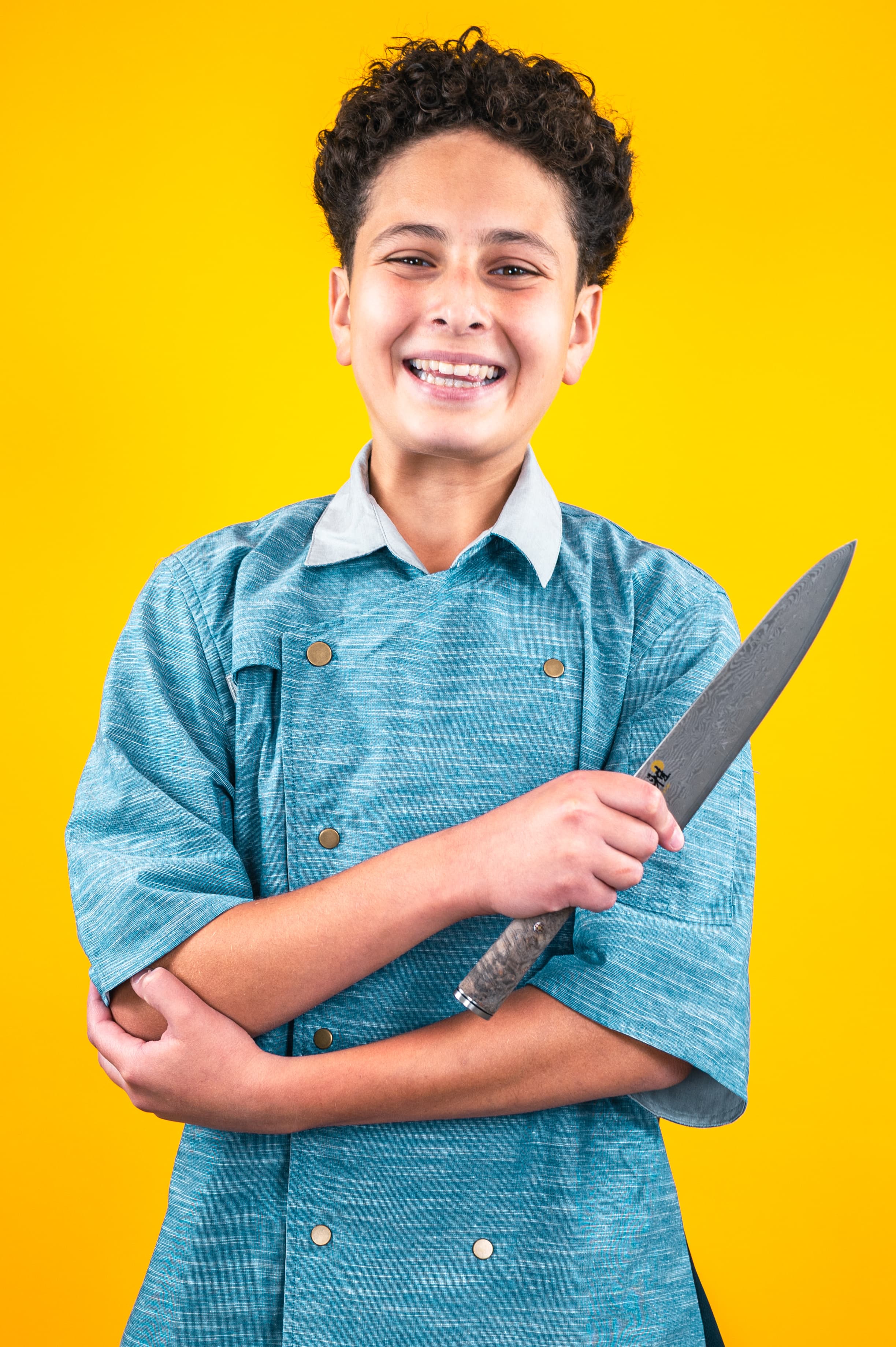 Nour in a chef coat holding a Damascus knife against an orange backdrop