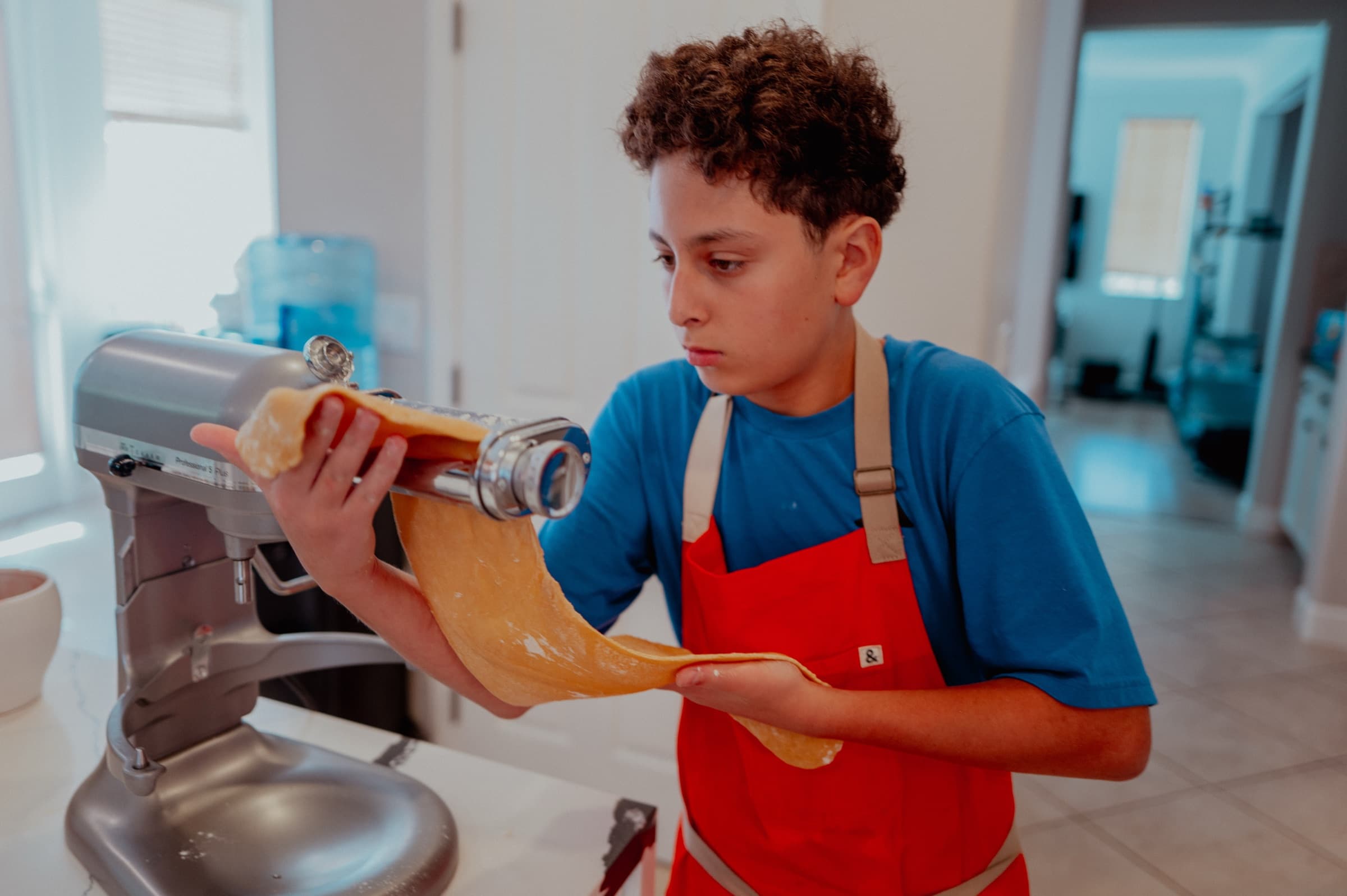 Nour rolling fresh pasta dough through a stand mixer attachment