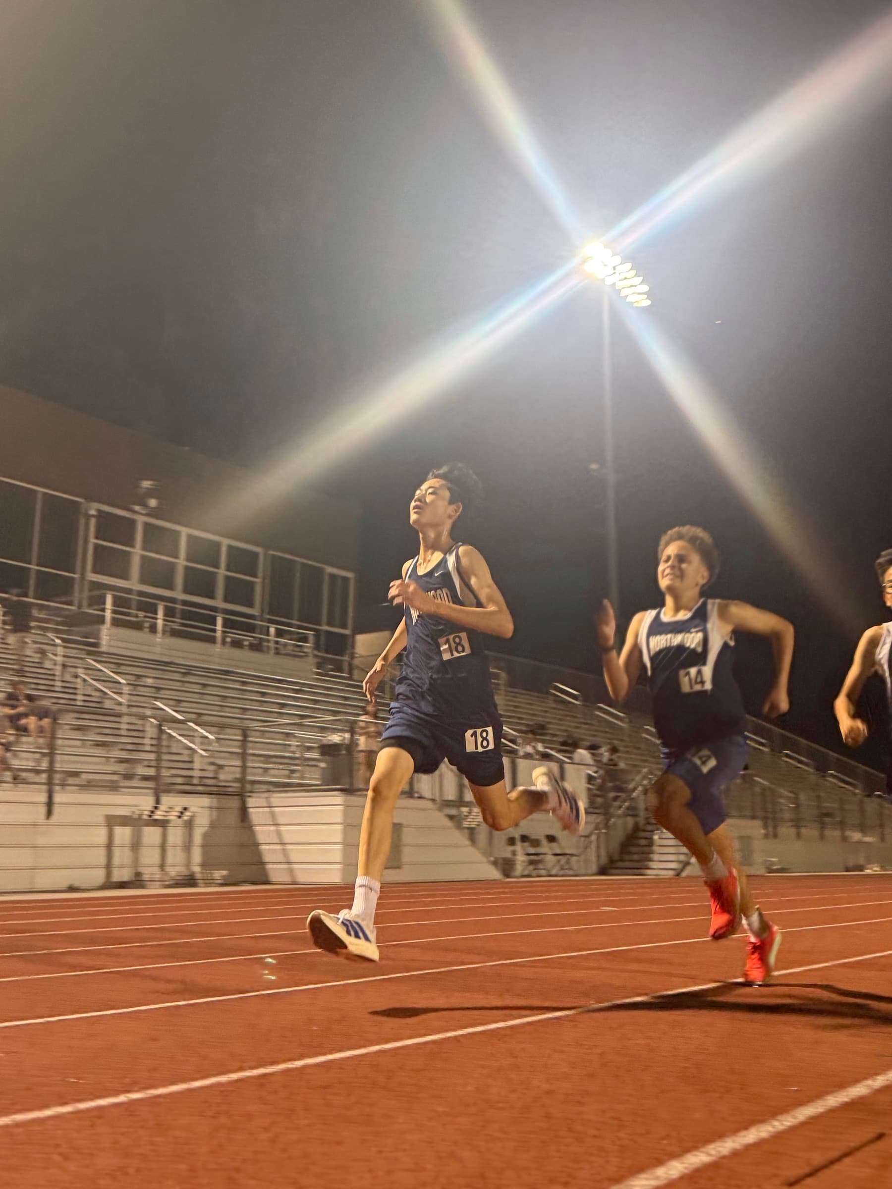 Two Northwood runners sprinting on a red track under stadium lights at night