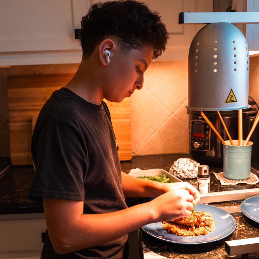 Nour plating chicken and rice under a kitchen heat lamp