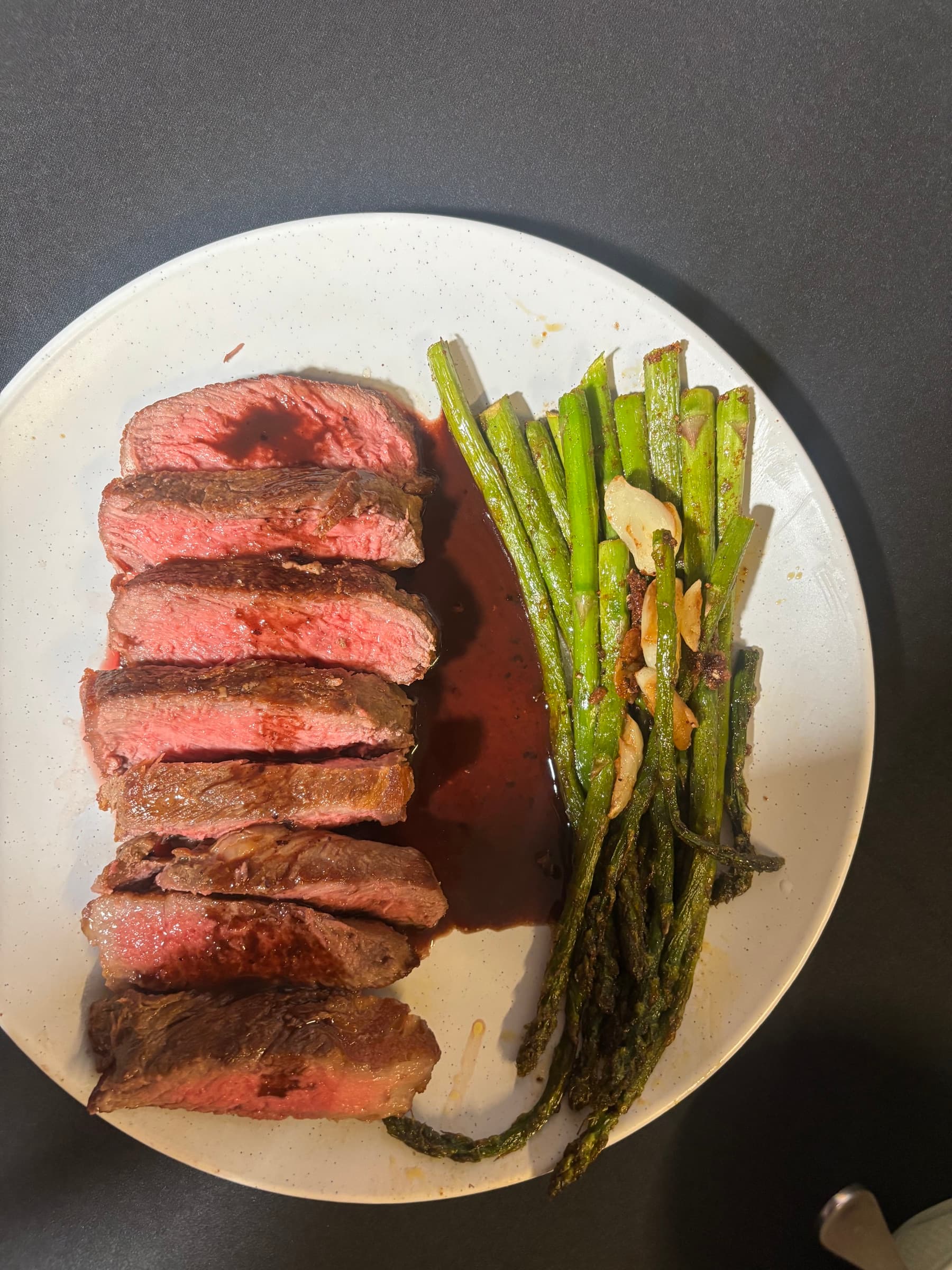 Sliced medium-rare steak with roasted asparagus on a speckled plate