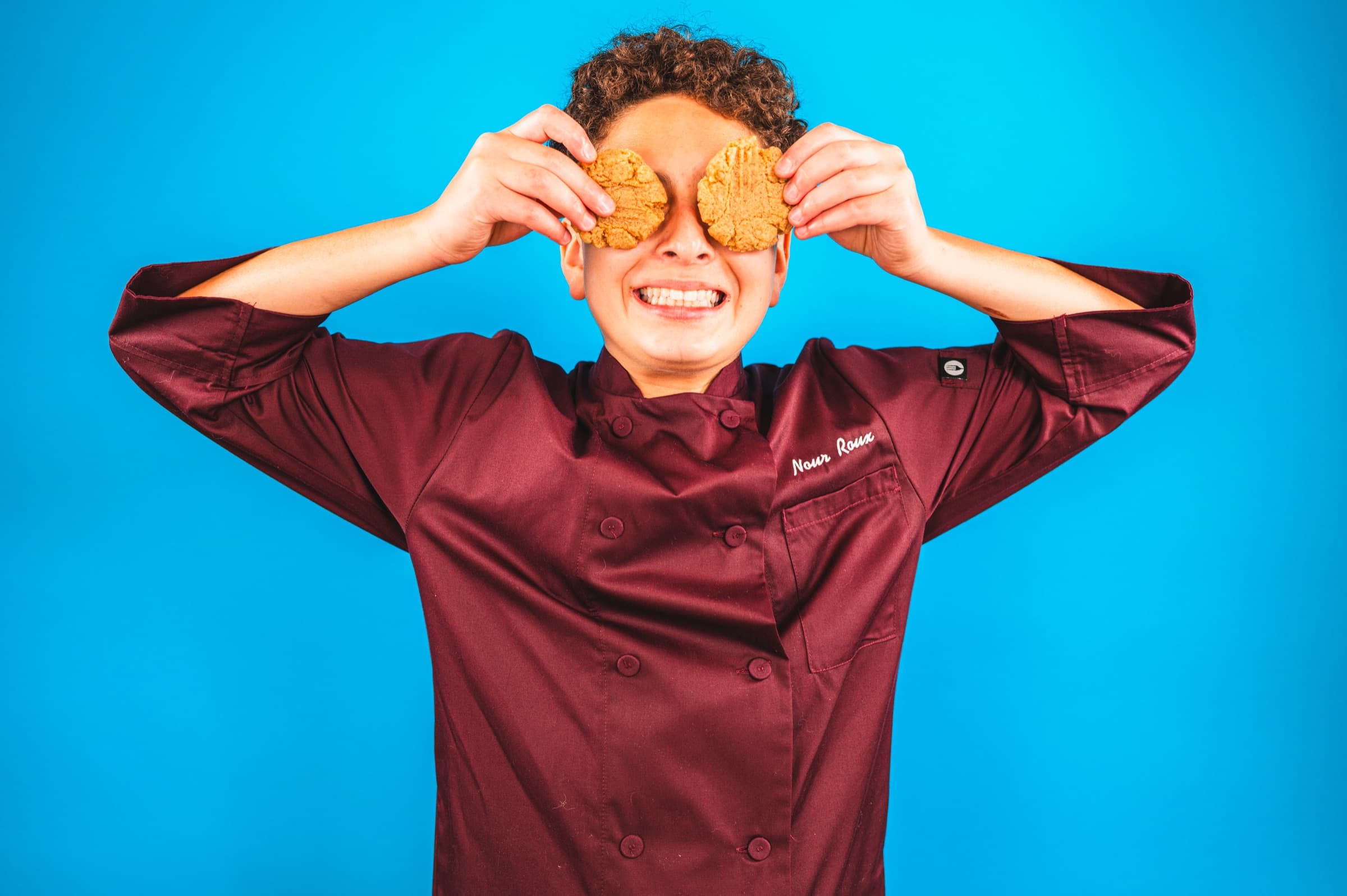 Nour in a chef coat holding cookies over his eyes